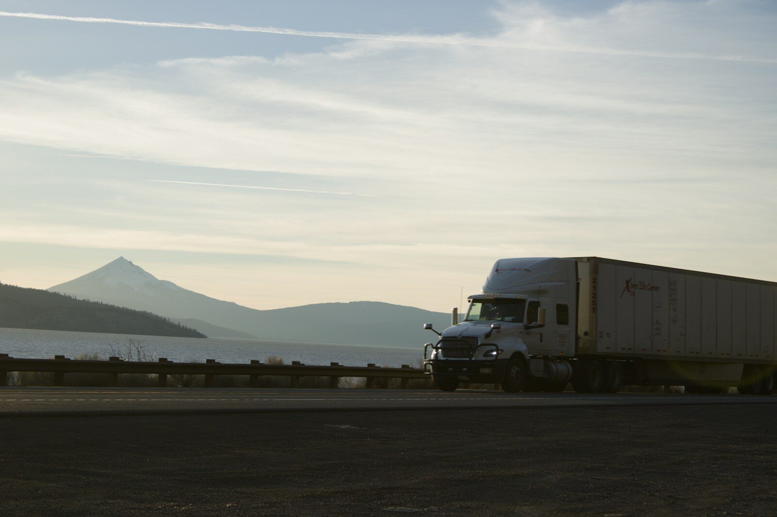A semi-truck drives along a scenic highway near mountains.